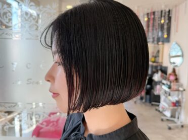 黒髪のタイトなミニボブをあごラインでぷつっと揃え、顔まわりをすっきり見せる前下がりシルエットと艶感が際立つ、La Senteのショートボブカットスタイル写真