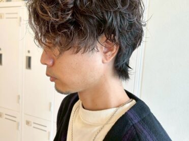 無造作なスパイラルパーマ風のミディアムショートを束感のある長め前髪で重ね、サイドはタイトに、襟足は程よく残してシルエットにメリハリをつけた、La Senteのメンズヘアスタイル写真