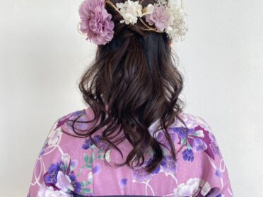 紫の花柄着物にネイビーの袴を合わせ、ゆる巻きのハーフアップにパープルと白のフラワー髪飾りを添えた、卒業式向けの後ろ姿ヘアアレンジ写真